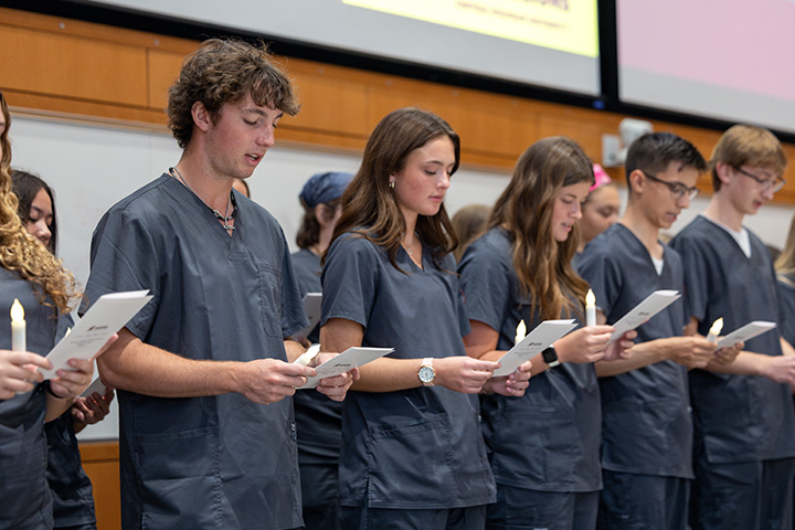 A group of nursing students stand at the front of a room reciting a pledge