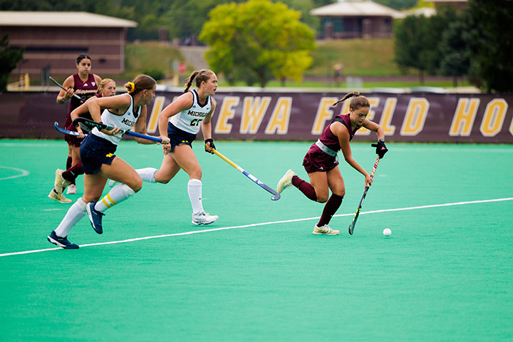 Female field hockey players run down the field during a game