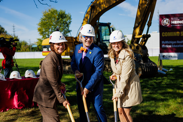 Three people hold shovels posing for a ceremonial groundbreaking event