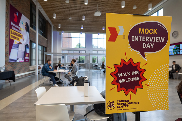 A sign reading Mock Interview Day with people sitting at a table in the background