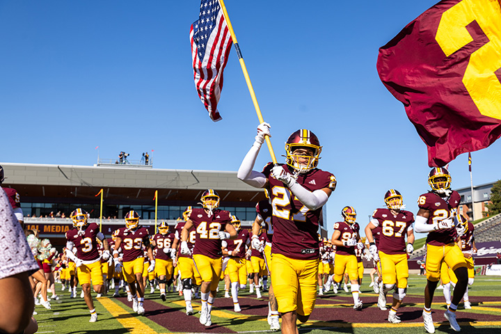 The CMU football team runs onto the field with one player waving a USA flag