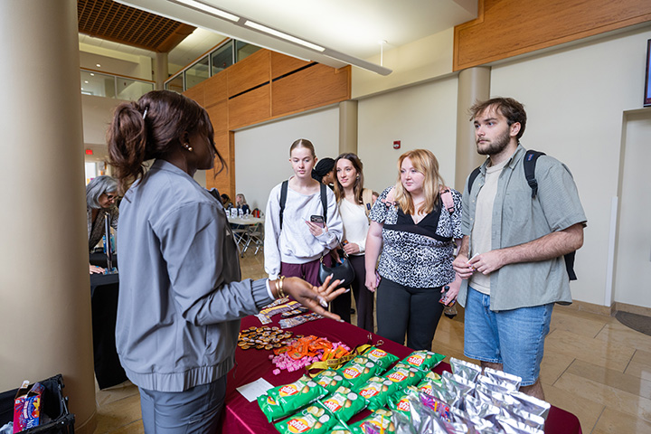 A group of four students stand in front of a table listening to another student discuss volunteer opportunities