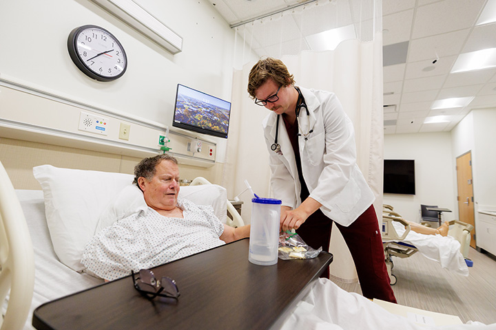 A CMU college of medicine student stands next to a patient in their hospital bed