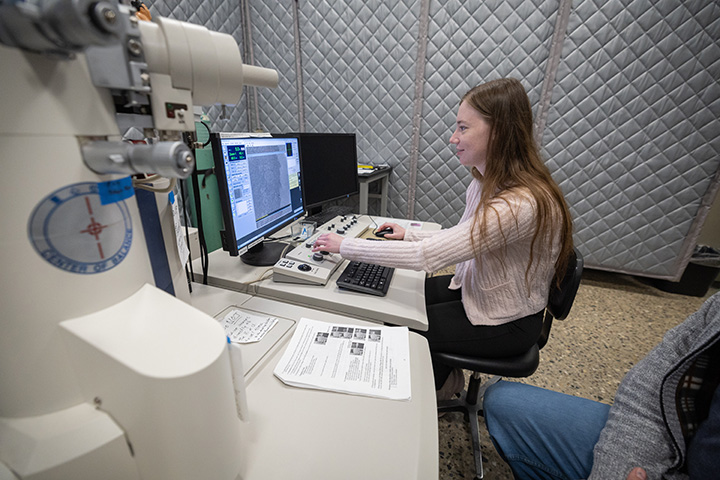 A student research sits at a computer screen controlling a large microscope