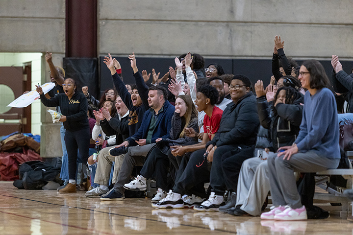 A group of people sitting on bleachers on the side of a basketball court.