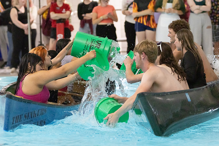 Students play a real life game of Battle Ship, sitting in small boats inside a pool while pouring buckets of water into their opponents' boat.