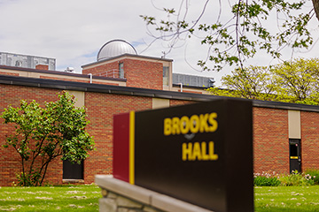 In the foreground, an out of focus sign reading Brooks Hall with the building in focus in the background