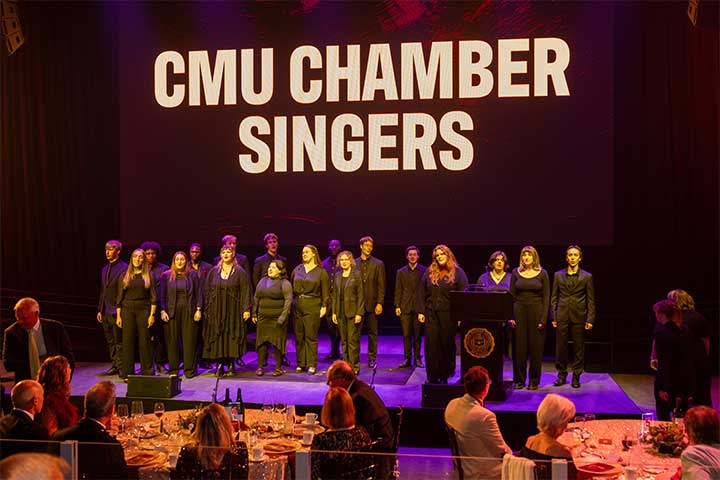 A group of men and women in dark colored clothing sing onstage