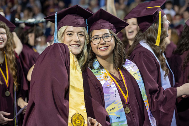 Two smiling women wearing maroon robes and caps.
