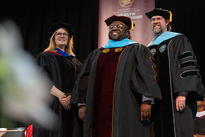 Three people wearing black robes smile while posing for a photo.