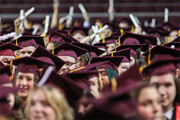 Smiling people wearing maroon caps and holding diplomas.