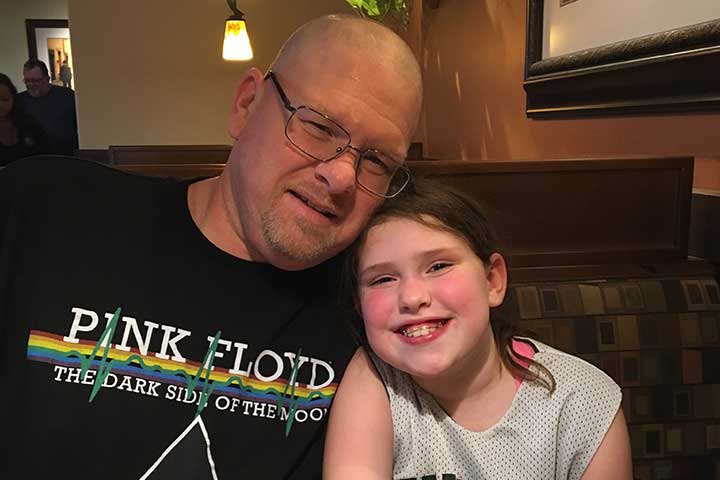 A bald man wearing glasses and his young brunette daughter sit in a restaurant booth