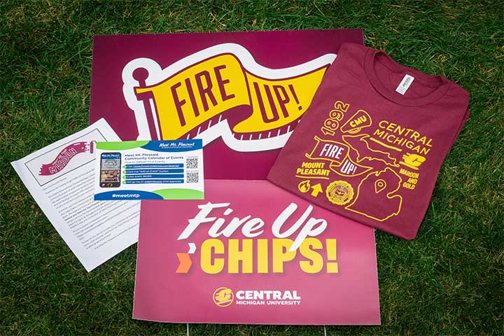 A maroon sign, t-shirt and sticker with the words Fire Up Chips lay in a neat pile on the grass