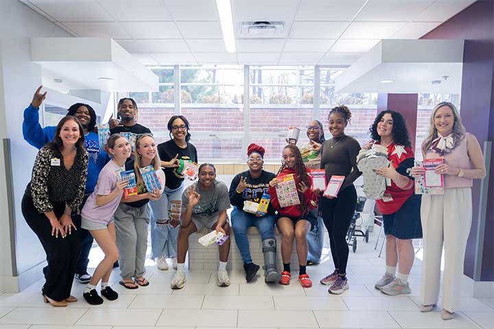 A group of diverse people pose with items donated for a charitable collection drive