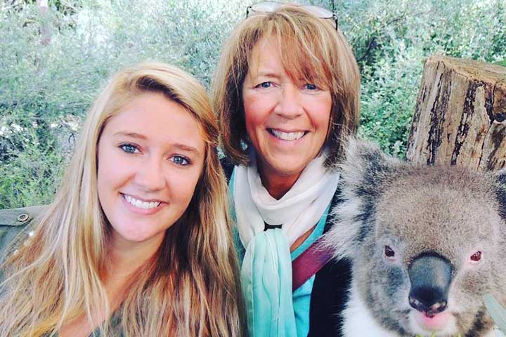 A young blond woman and an older woman in glasses pose with a koala bear