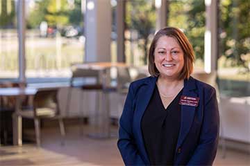 A brunette woman in a blue suit jacket smiles for the camera
