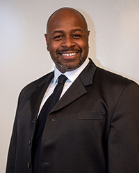 A man in a black suit and tie smiling at the camera