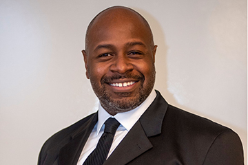 A man in a black suit and tie smiling at the camera