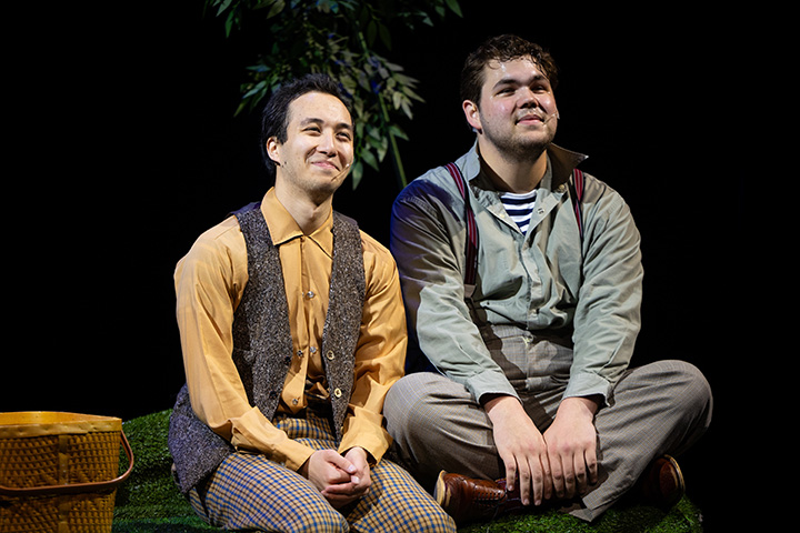 Two young men wearing vintage clothing sit in chair smiling looking off the right side of the image