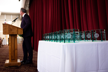 A group of trophies on a table next to a man speaking at a podium.