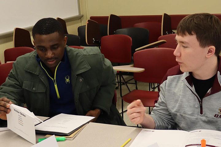 Two students sit at a desk in a classroom