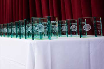 Numerous glass awards featuring the CMU seal sit in neat rows atop a white tablecloth