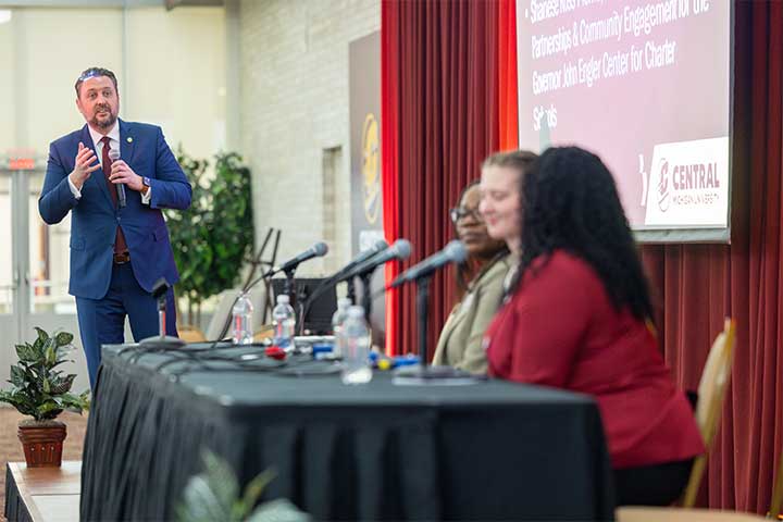 A man in a blue suit moderates a panel discussion in front of a red velvet curtain
