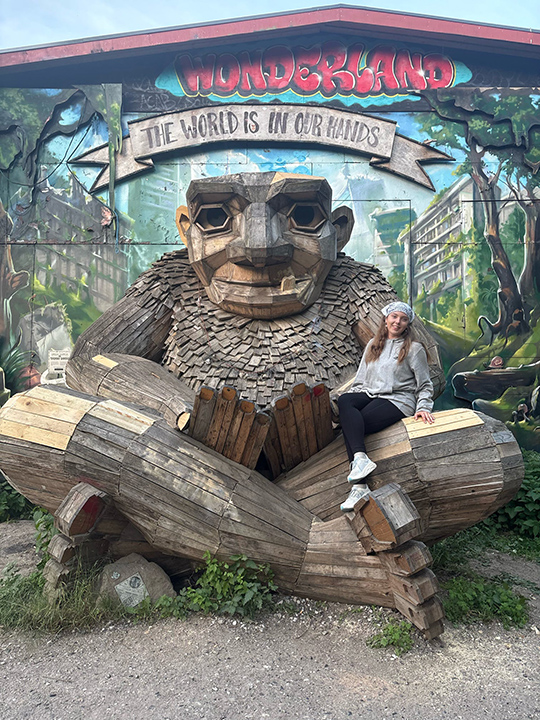 A female CMU student sits on the lap of a very large wooden statue
