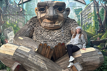 A female CMU student sits on the lap of a very large wooden statue