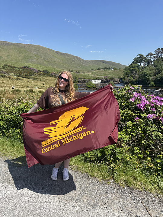 A female college student holding a CMU flag while standing outside in Copenhagen