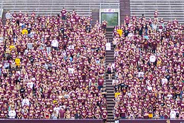 A crowd of students wearing maroon tshirts stands in the CMU stadium