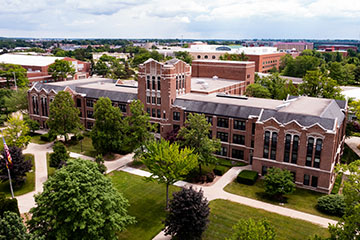 Aerial view of Warriner Hall on CMU's campus, capturing clouds in the sky, green grass, trees, and sidewalks from above.