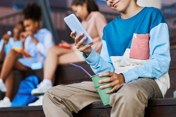 Elementary and middle school-aged children look at their phones while sitting on bleachers in a gymnasium