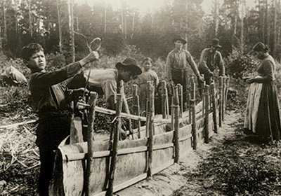 Historical black and white photo of Native Americans making a canoe