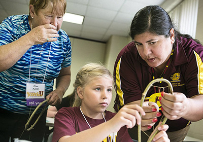 Two women showing a young girl how to make an Indigenous craft during GrandParents U event