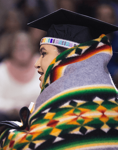 Native American student wears her cap and gown and traditional celebration colors at Central Michigan University's Commencement.