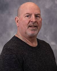 Tim Theisen, Counselor. Profile headshot wearing a black long sleeve shirt and a grey background.