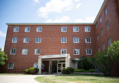 Front entrance of Thorpe Hall with glass doors, curved canopy, and small shrubs near the walkway.