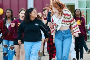 A group of students walking together, smiling and happy as they walk wearing maroon and gold.