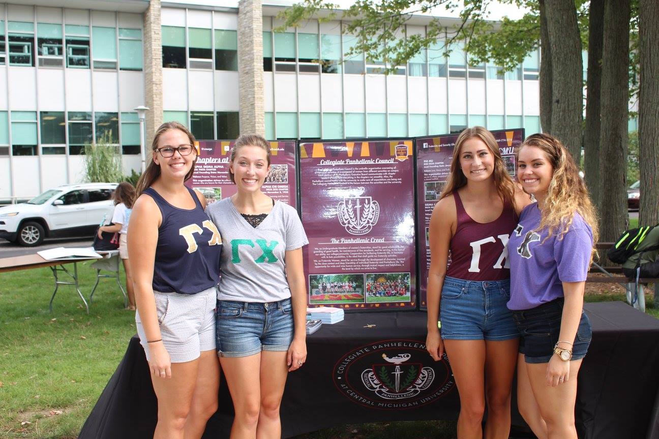 Four young women in shorts and t-shirts standing outside in front of a display table.