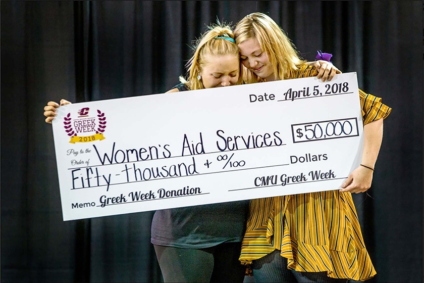 Two women embrace while holding an over-sized donation check of $50,000.