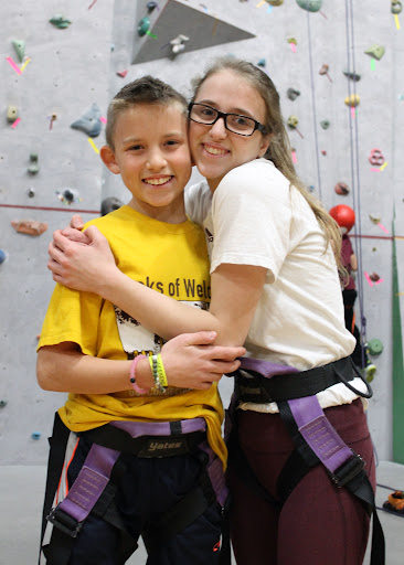 Two people standing in front of a rock climbing wall and smiling.