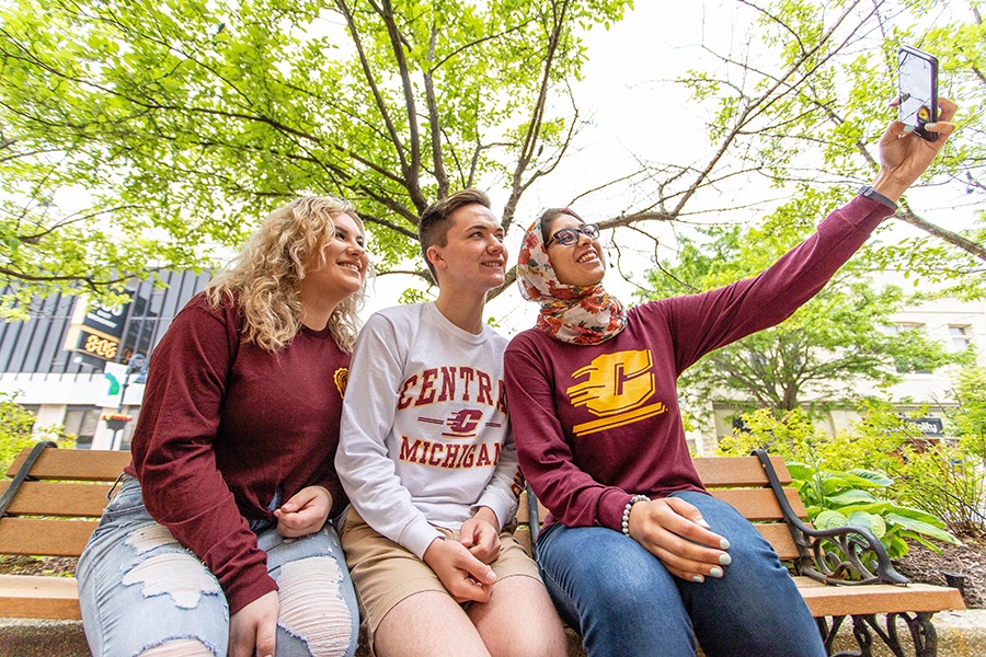 Three students on a bench in downtown Mt. Pleasant taking a selfie