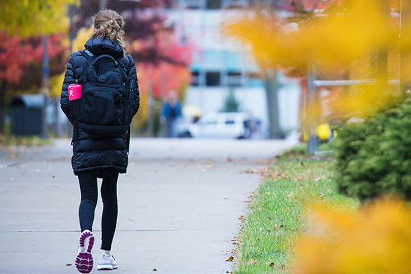 A student wearing a black coat and backpack walks on campus.