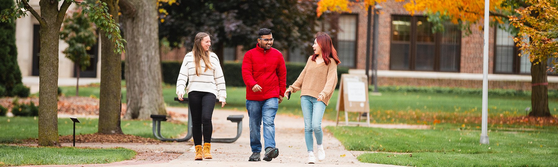 2 female students and 1 male student walking outside on campus in the fall.