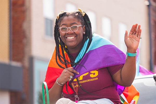 Black woman wrapped in a rainbow flag waiving to camera