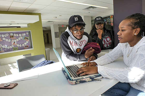 Three black students working on a laptop computer.