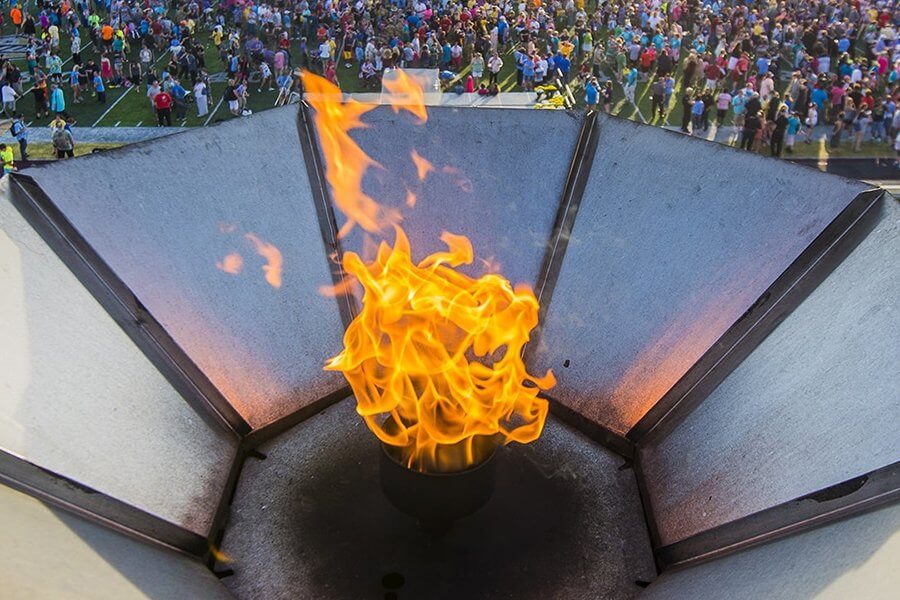 A close up of the Special Olympics flame in the stands with people on the football field in the background.