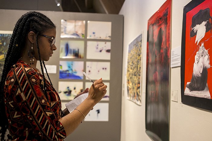 A woman taking notes on one of the paintings in the Mitli Mitlak Reception at the Central Michigan University Art Gallery.
