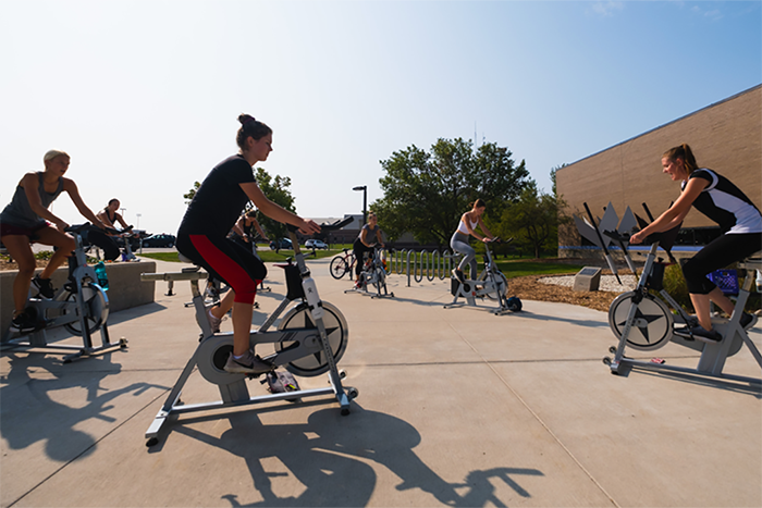A group of students using stationary bikes outside of the Student Activity Center (SAC) while being instructed.